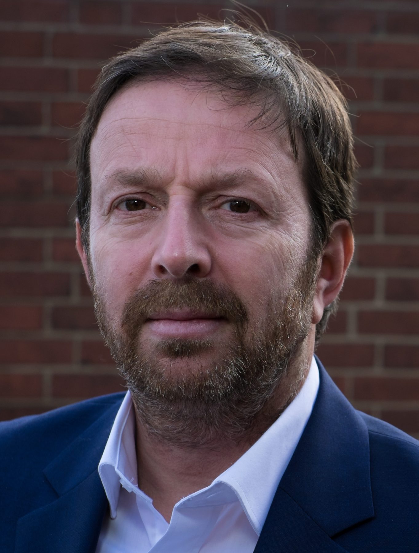 Portrait of Mark Maier in a navy jacket against a brick wall
