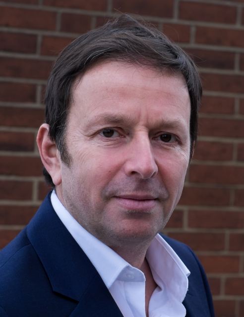 Head and shoulders portrait, navy suit, brick wall