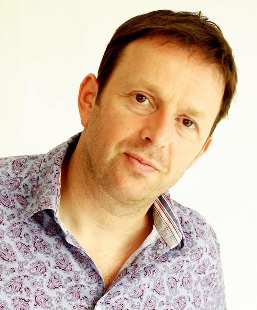 Publicity portrait in a paisley shirt, head tilted