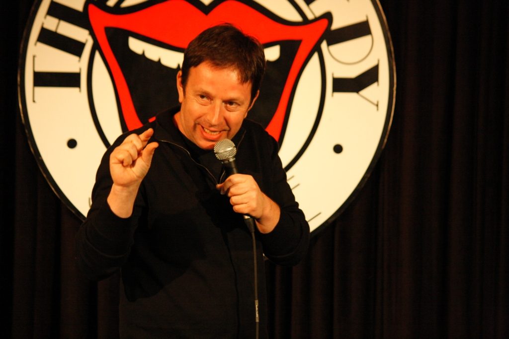 Mark Maier on stage, pointing at the audience with microphone in hand